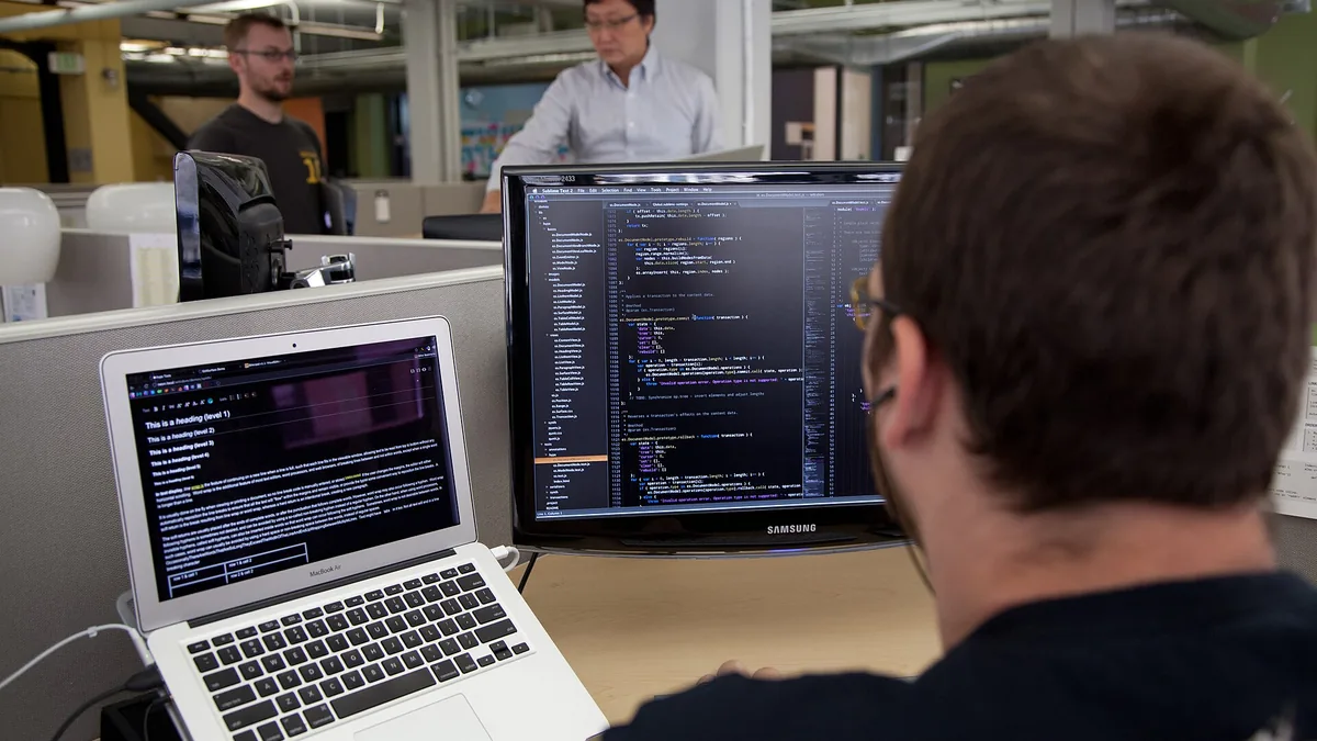 Trevor Parscal coding in the Wikimedia Foundation offices. The image shows the back of a bearded brunette caucasian male with glasses wearing earphones in front of two screens and keyboards